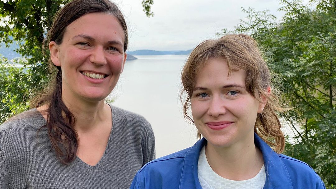 Två kvinnor ler mot kameran med kust i bakgrunden