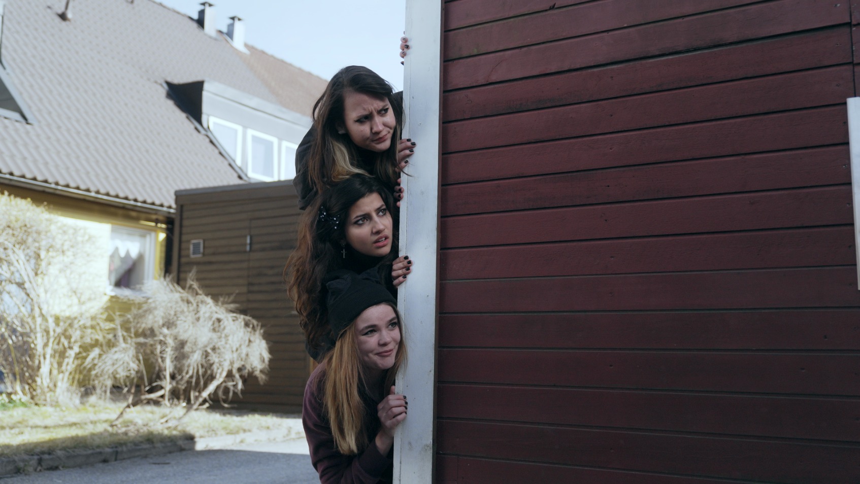 tre flickor tittar fram bakom ett stughörn.
