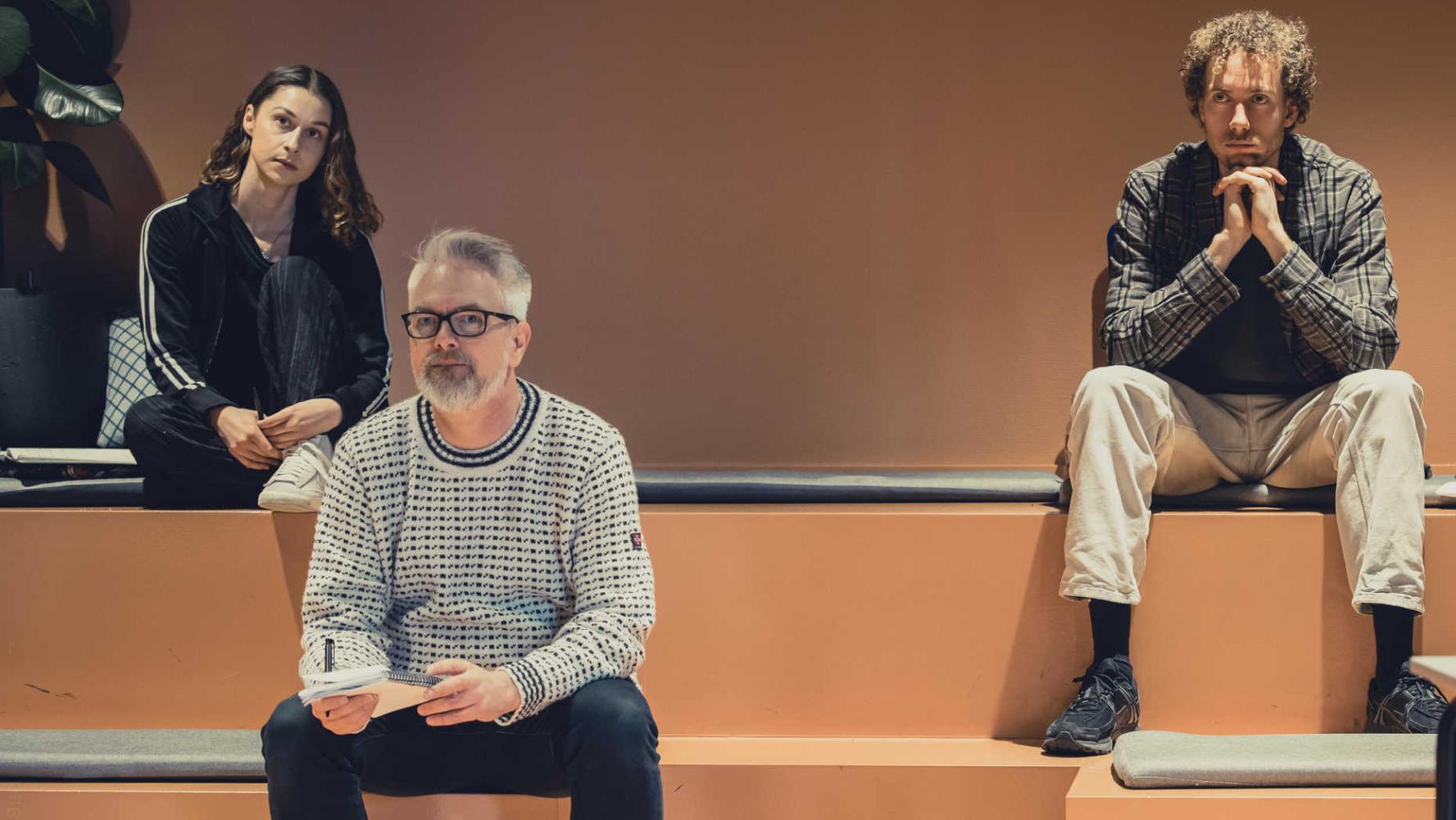 Tre personer sitter på en läktare och tittar koncentrerat