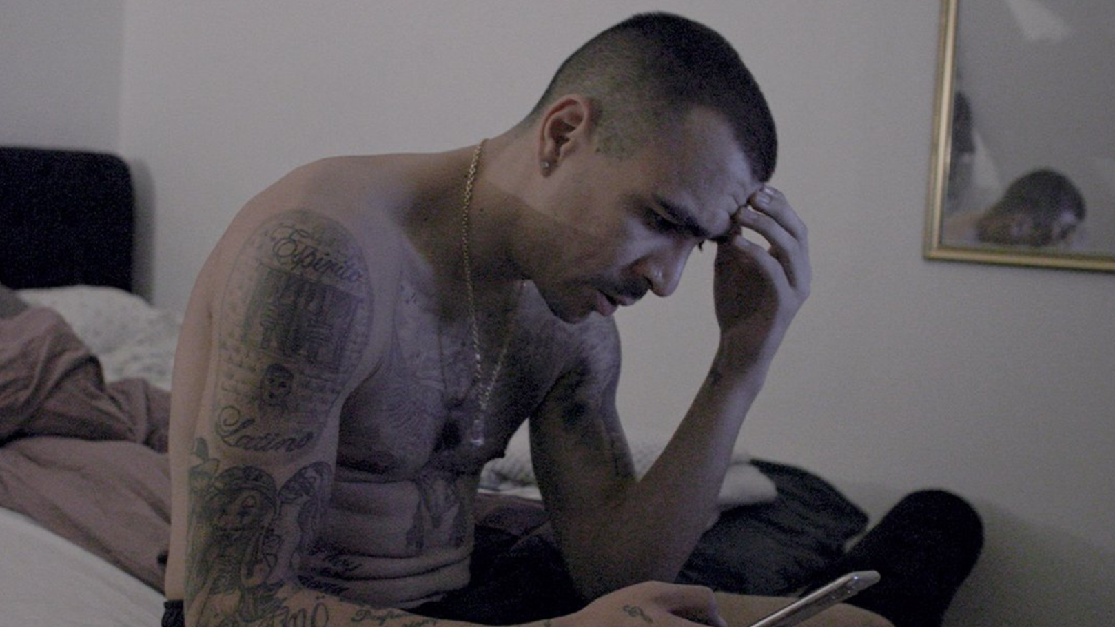 Man sitter med bekymrad blick på en säng och tittar i en telefon.