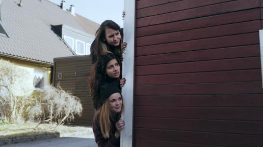 tre flickor tittar fram bakom ett stughörn.