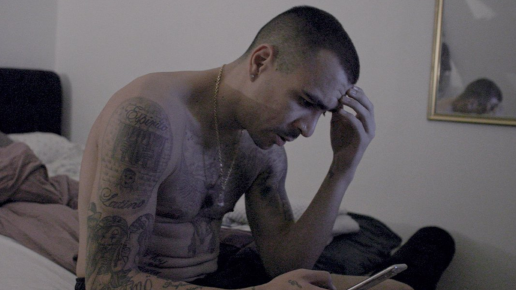 Man sitter med bekymrad blick på en säng och tittar i en telefon.