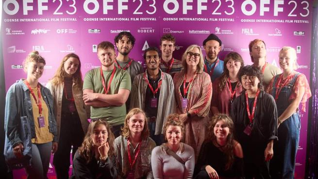 Grupp med filmskapare framför festivalfotovägg
