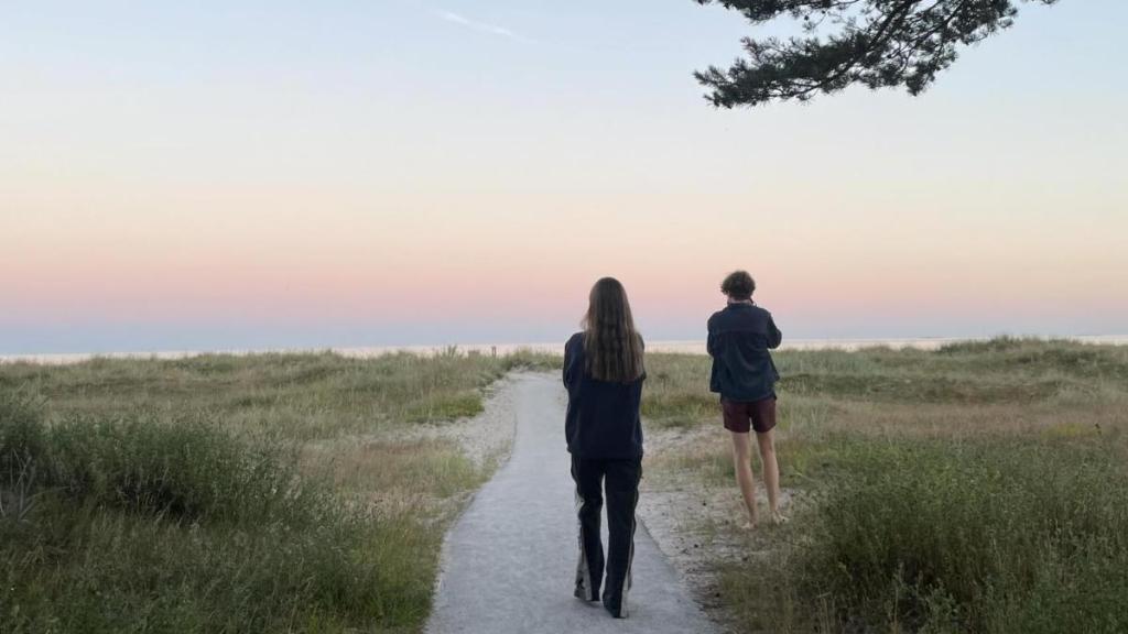 Två sommarklädda på gångväg mot en sandstrand